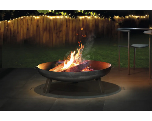 Brasero avec du bois qui brûle dans un jardin.