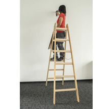 Femme debout sur une échelle en bois perçant un mur avec une perceuse