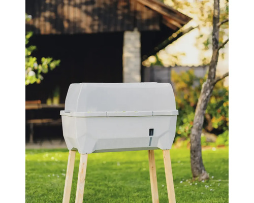 Komposter aus Kunststoff mit Holzbeinen im Garten.