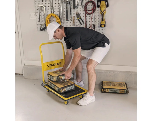 Mann lädt Säcke mit Betonmischung auf einen gelben Transportwagen von Stanley