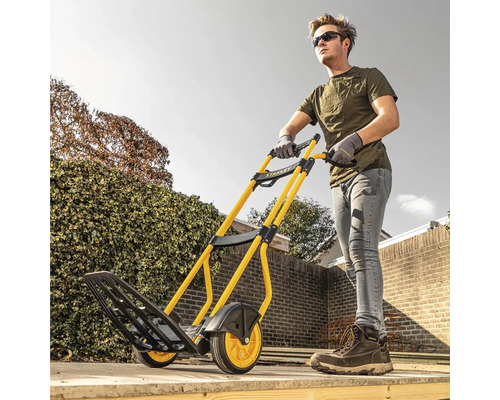 Homme poussant un diable jaune et noir de Stanley dans le jardin.