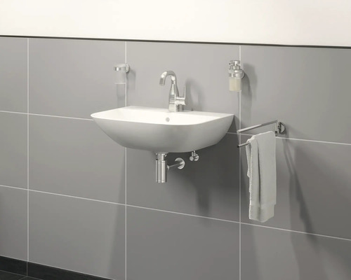 Waschbecken mit Armatur, Handtuchhalter, Seifenspender und Zahnputzbecher an einer grauen Wand