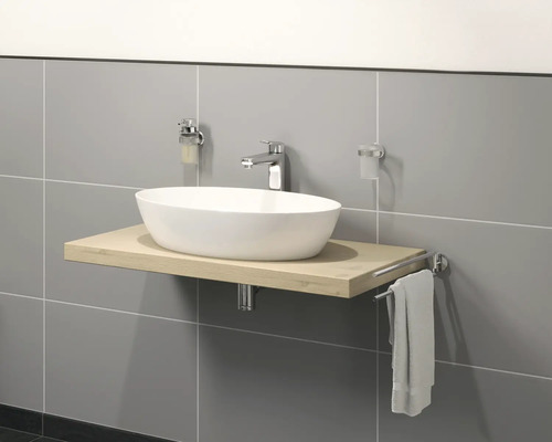 Lavabo sur plaque de bois avec robinetterie, distributeur de savon, gobelet à brosse à dents et porte-serviettes devant un mur gris