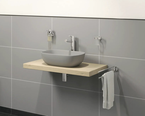 Meuble de salle de bains avec lavabo à poser, robinetterie, distributeur de savon, gobelet à brosse à dents et porte-serviettes devant un mur carrelé