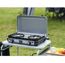Doppelgaskocher auf einem Campingtisch im Freien mit geöffnetem Deckel.