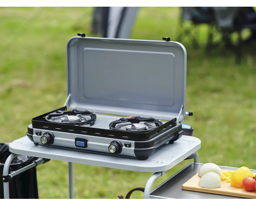 Doppelgaskocher auf einem Campingtisch im Freien mit geöffnetem Deckel.