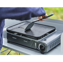 Campingtischgrill mit Grillplatte und Person mit einem Spatel