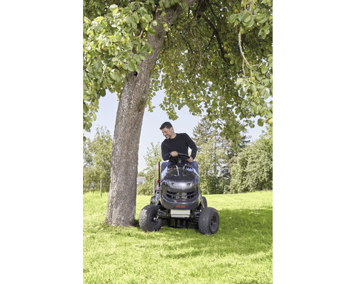 Un homme conduit un tracteur de pelouse sur une pelouse autour d''un arbre.