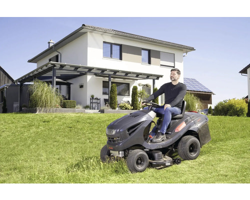 Homme sur tracteur de pelouse tondant la pelouse devant une maison