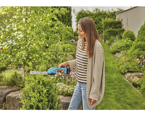 Une femme coupe une haie avec un taille-haie sans fil dans un jardin.