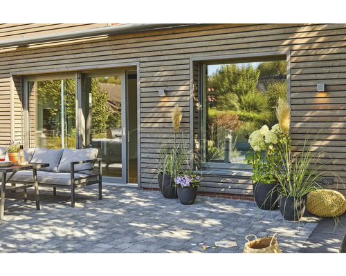 Terrasse mit Steinpflaster, Gartenmöbeln, Pflanzen und Holzfassade