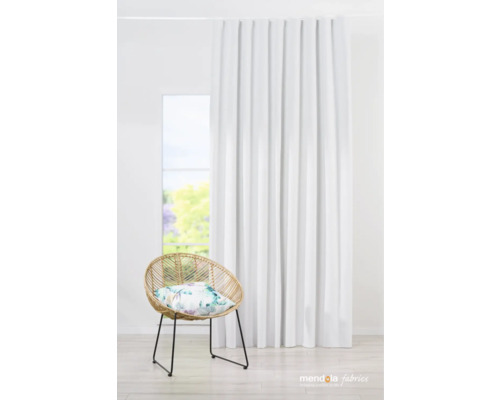 Innenaufnahme eines Wohnraums mit weißem Vorhang, Rattansessel und floralem Kissen vor einem Fenster