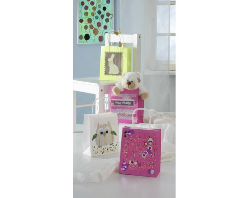 Sacs cadeaux décorés dans différents designs avec un ours en peluche sur une chaise blanche.