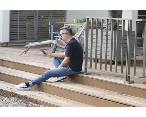 Un homme est assis sur une terrasse en bois et utilise un smartphone