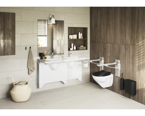 Badezimmer mit Doppelwaschtisch, Spiegel, Toilette mit Haltegriffen und Ablagefächern.