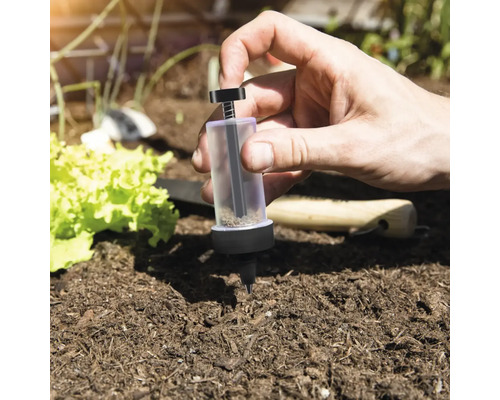 Personne utilisant un distributeur de semences dans un parterre de jardin