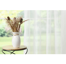 Fleurs séchées décoratives dans un vase blanc sur une petite table devant une fenêtre avec un rideau.