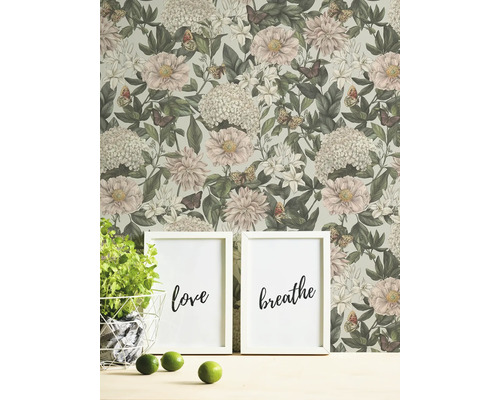 Wohnszene mit Blumentapete, zwei gerahmten Bildern mit den Aufschriften Liebe und Atmen, Topfpflanze und Limetten