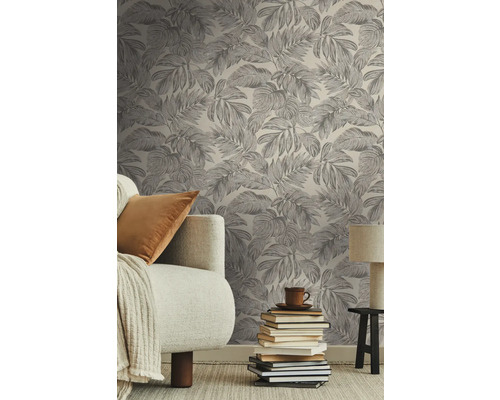 Wohnzimmer mit einer mit Blättern bedruckten Tapete, einem Sofa, einem Stapel Bücher und einer Lampe.