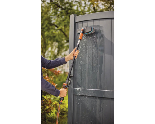 Une personne nettoie une clôture en bois avec une brosse et un tuyau.