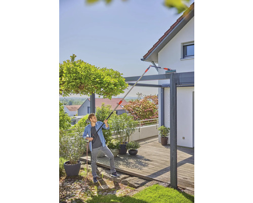 Un homme nettoie un toit de terrasse avec une perche télescopique et un tuyau d''arrosage.