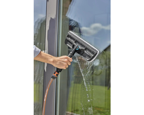 Une personne nettoie une fenêtre avec un lave-vitre et un tuyau d''arrosage.