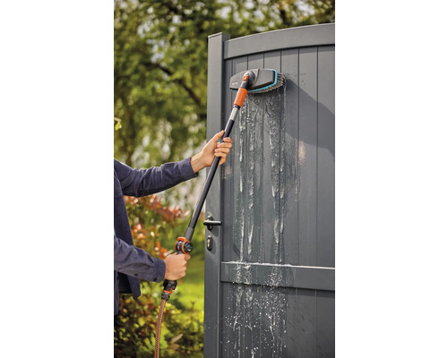 Personne nettoyant un portail de jardin avec une brosse de lavage à manche télescopique