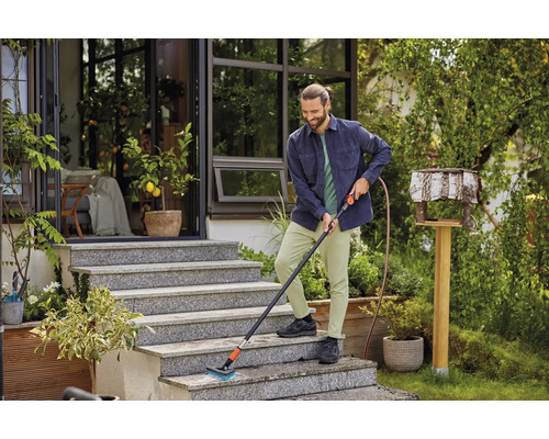 Un homme nettoie un escalier extérieur avec une brosse et un raccord d''eau