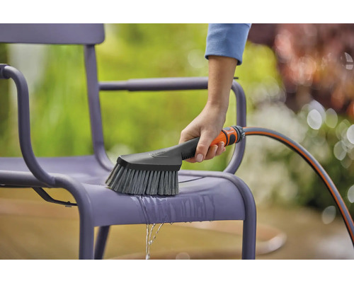 Nettoyage d''une chaise de jardin avec une brosse et un tuyau d''arrosage.