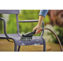 Une personne nettoie une chaise de jardin avec une brosse et un tuyau d''arrosage.