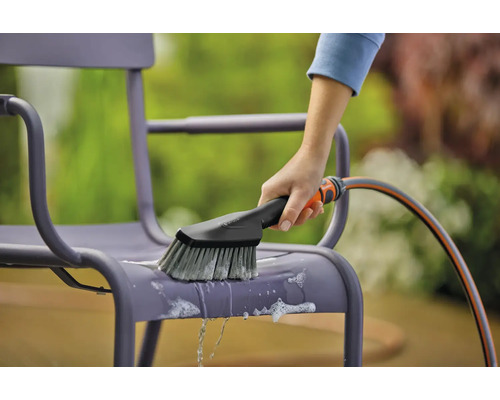 Une personne nettoie une chaise de jardin avec une brosse et un tuyau d''arrosage.
