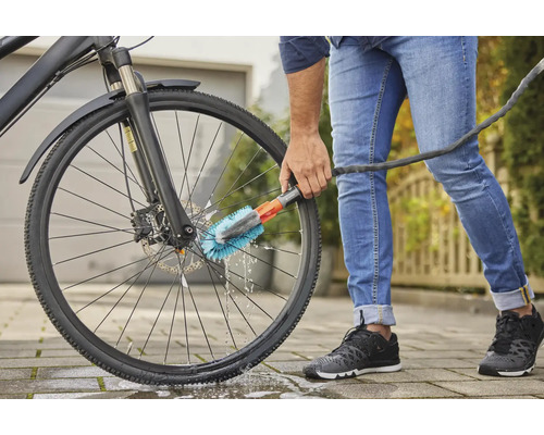 Une personne nettoie un vélo avec une brosse et un tuyau d''arrosage.
