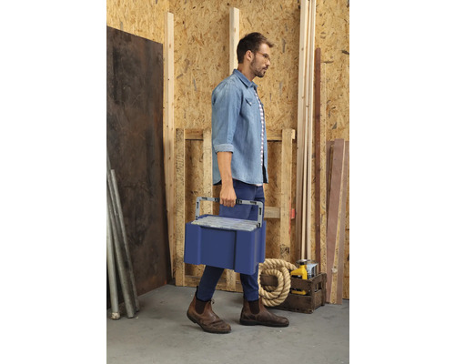 Un homme transporte une boîte à outils bleue dans un atelier