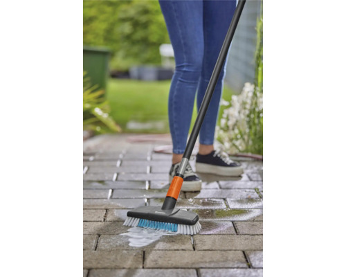 Une personne nettoie le pavage avec une brosse et un manche à l''extérieur.
