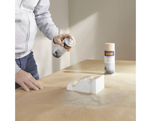 Eine Person sprüht eine Zierleiste mit Strukturspray.