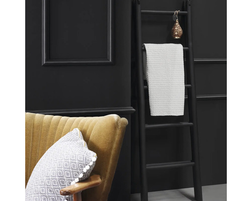 Scène décorative avec échelle, serviette, fauteuil et coussin sur fond sombre.