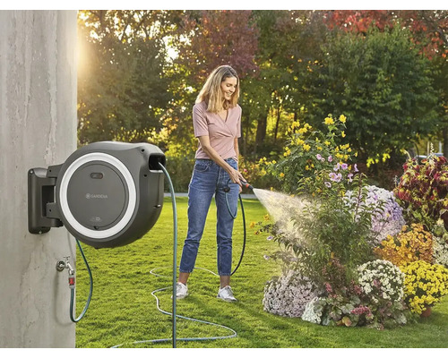Frau bewässert Blumen mit einer an der Wand montierten Schlauchtrommel im Garten