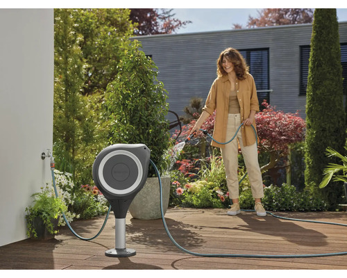 Scène de jardin avec une femme utilisant un tuyau d''arrosage sortant d''un coffre de tuyau avec support