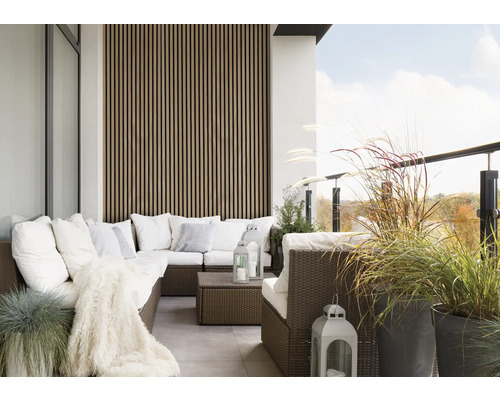 Balkon mit Rattansitzgruppe, Kissen, Decke, Laternen und Pflanzenkübeln.