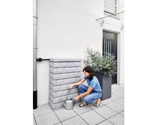 Une femme remplit un arrosoir à partir d''une cuve de récupération d''eau de pluie dans le jardin.