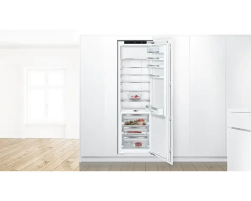 Réfrigérateur encastrable ouvert avec des aliments dans une cuisine claire.