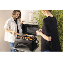 Deux femmes grillent des légumes et de la viande sur un barbecue portable à l''extérieur.