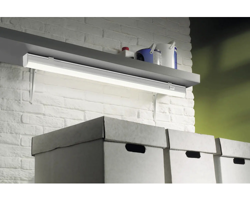 Étagère avec luminaire sous meuble, pots de peinture et boîtes de rangement devant un mur de briques