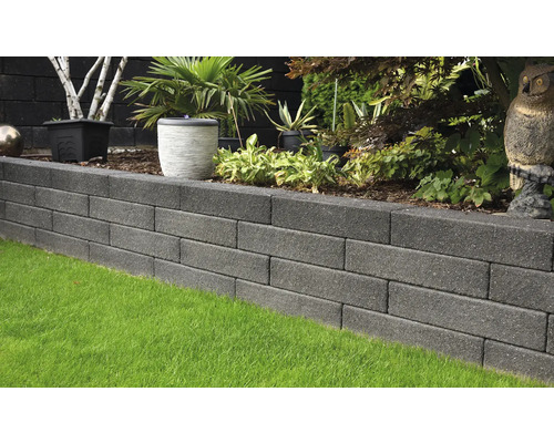 Muret de jardin en blocs de béton avec pelouse au premier plan et plantes à l''arrière-plan.