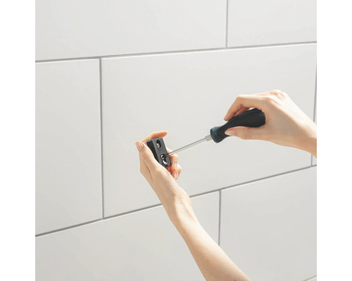 Une personne fixe un support à un mur carrelé avec un tournevis.