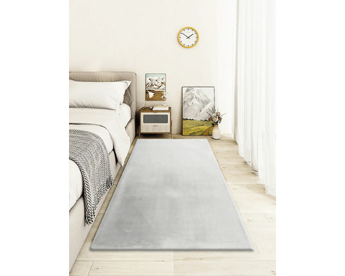 Chambre avec lit, table de chevet et tapis gris sur plancher en bois.