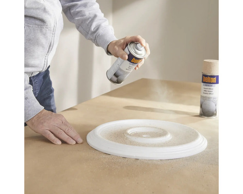 Une personne vaporise une bombe de peinture sur une rosace de plafond.