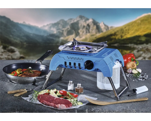 Campingkocher mit angebratenem Steak, Gemüse und Zutaten vor Bergkulisse