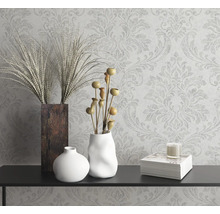 Nature morte décorative avec vases, plantes ornementales, bougie et livre sur une console devant un papier peint à motifs