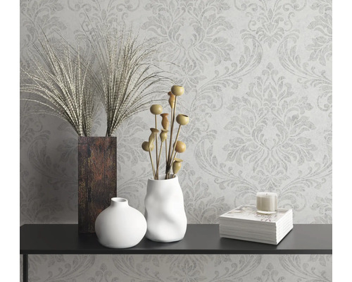 Nature morte décorative avec vases, plantes ornementales, bougie et livre sur une console devant un papier peint à motifs